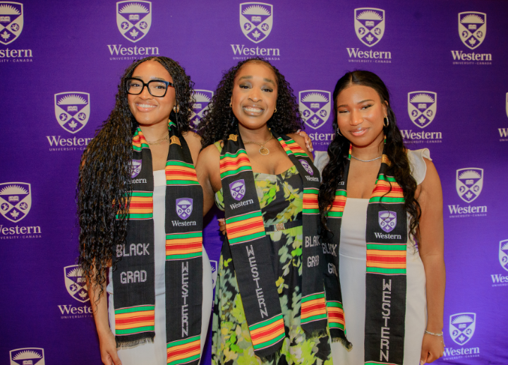 Three Black graduates posing for the camera in front of a Western purple backdrop
