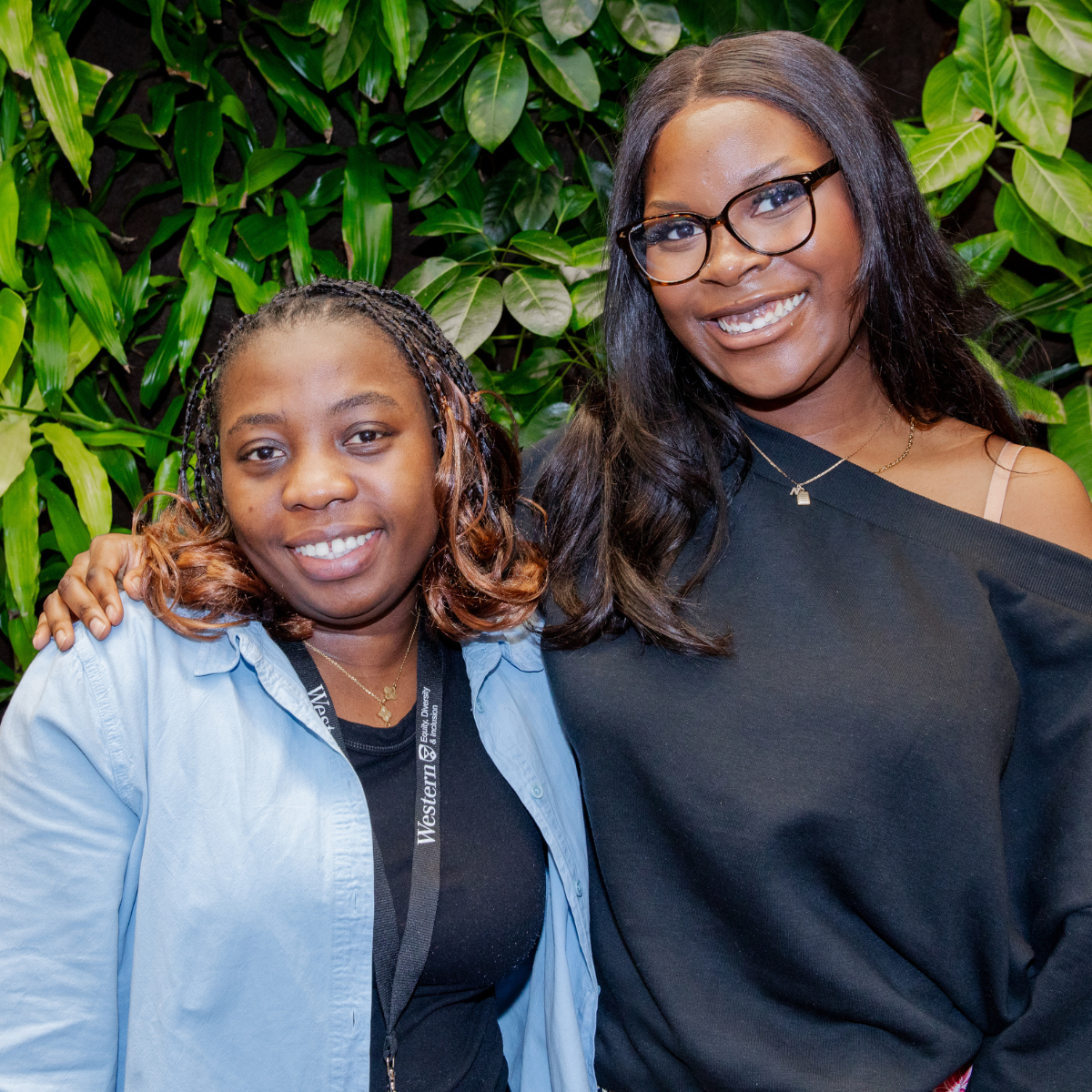 Two women smiling in front of a green plant wall