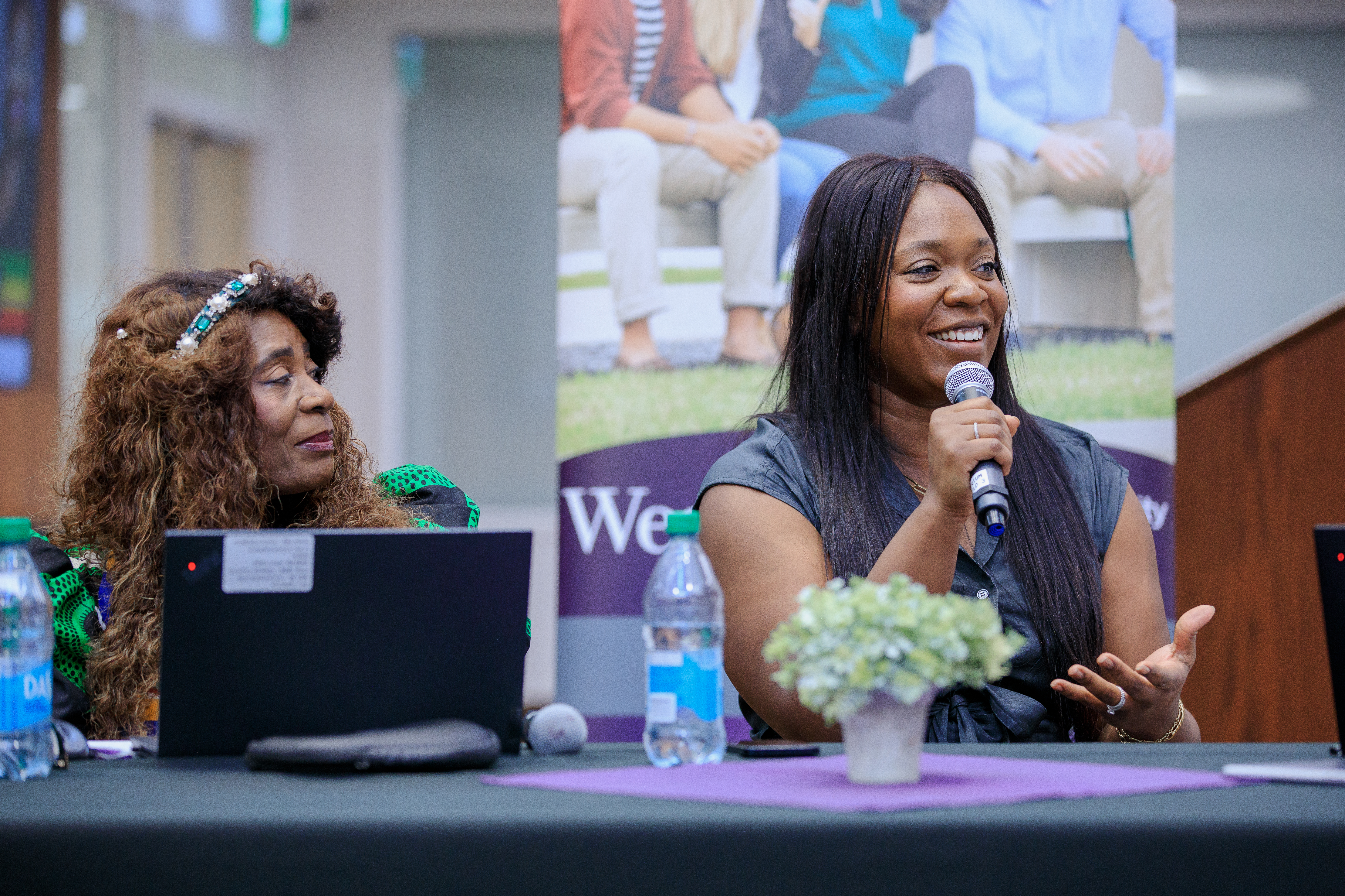 This is a photo of the Black Resistance Against the Status Quo Panel event on February 24, 2025. This photo features Chief Commissioner of the Ontario Human Rights Commission, Patricia DeGuire and Music Director and Lead Activist for Black Lives Matter London Alexandra Kane. Alexanra Kane is speaking into a microphone while sitting at a table. 
