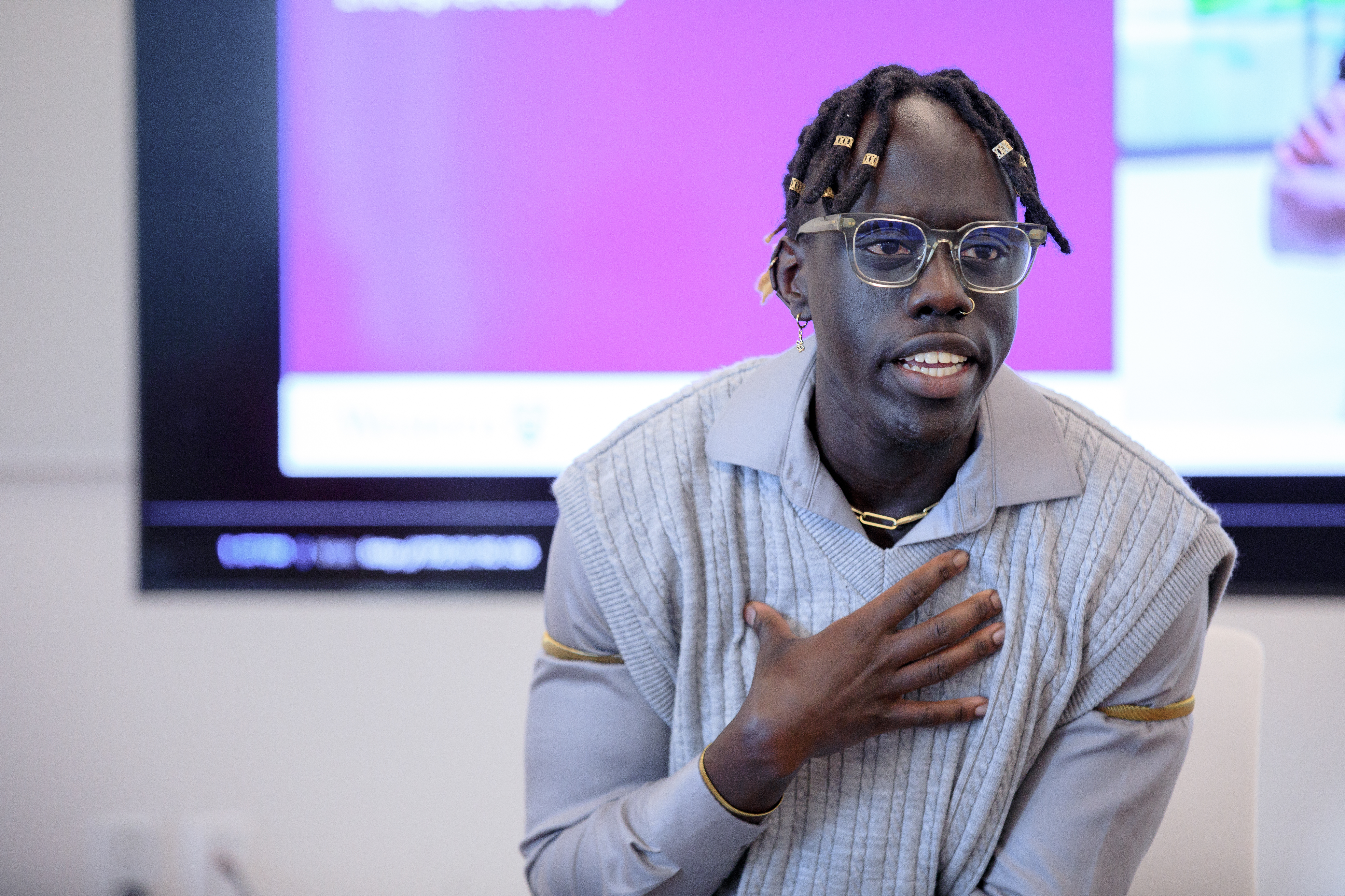 Former USC President Sunday Ajak talks to a group of people at the Being Black with a Purpose: Black Resistance and Leadership in Action event on February 26, 2025. Sunday is wearing glasses, a grey shirt and knitted vest, holding his hand to his chest. 
