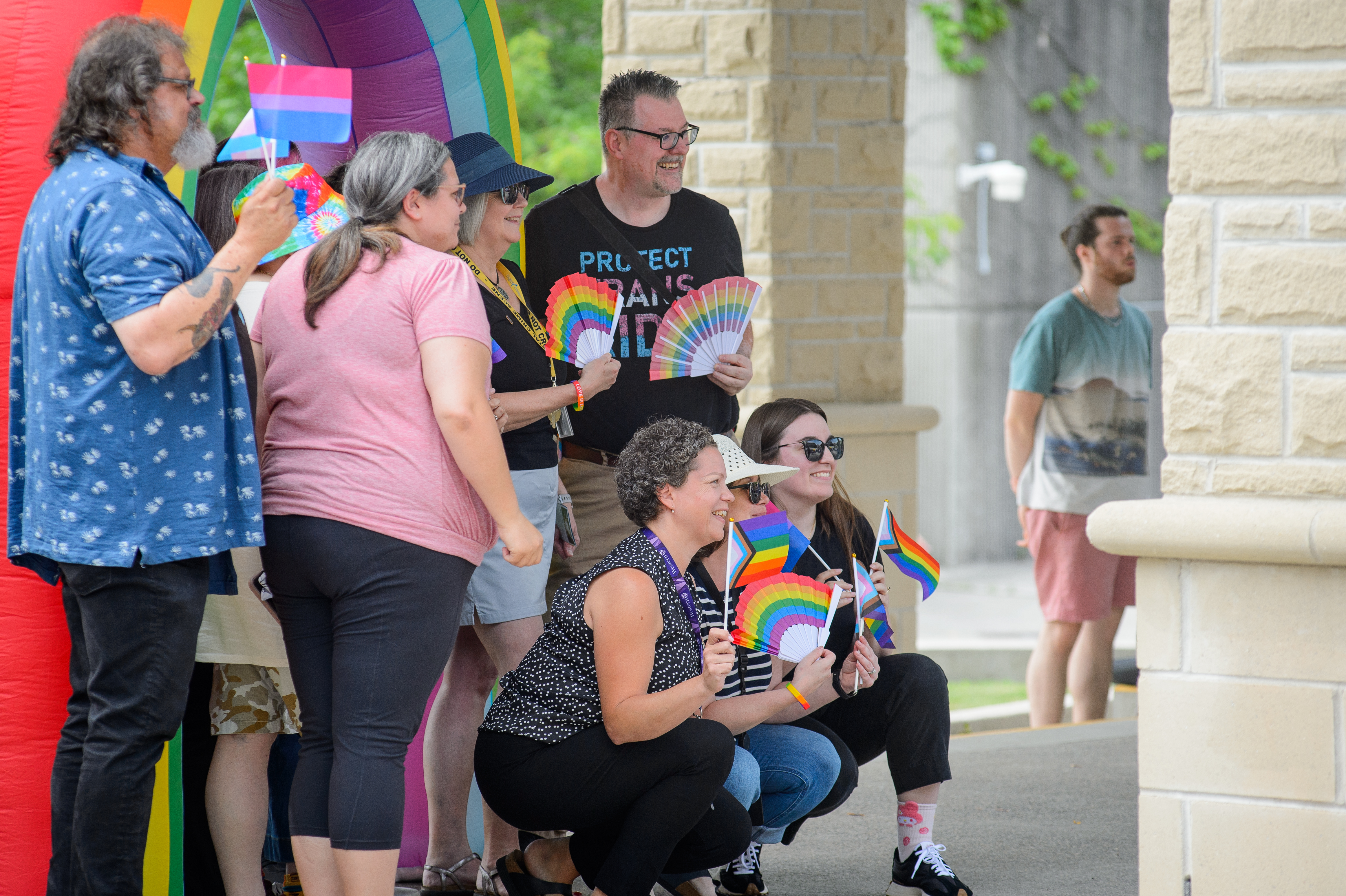 A group of people pose for a photo in front of a rainbow for Pride on Concrete Beach, this image is taken from the side.