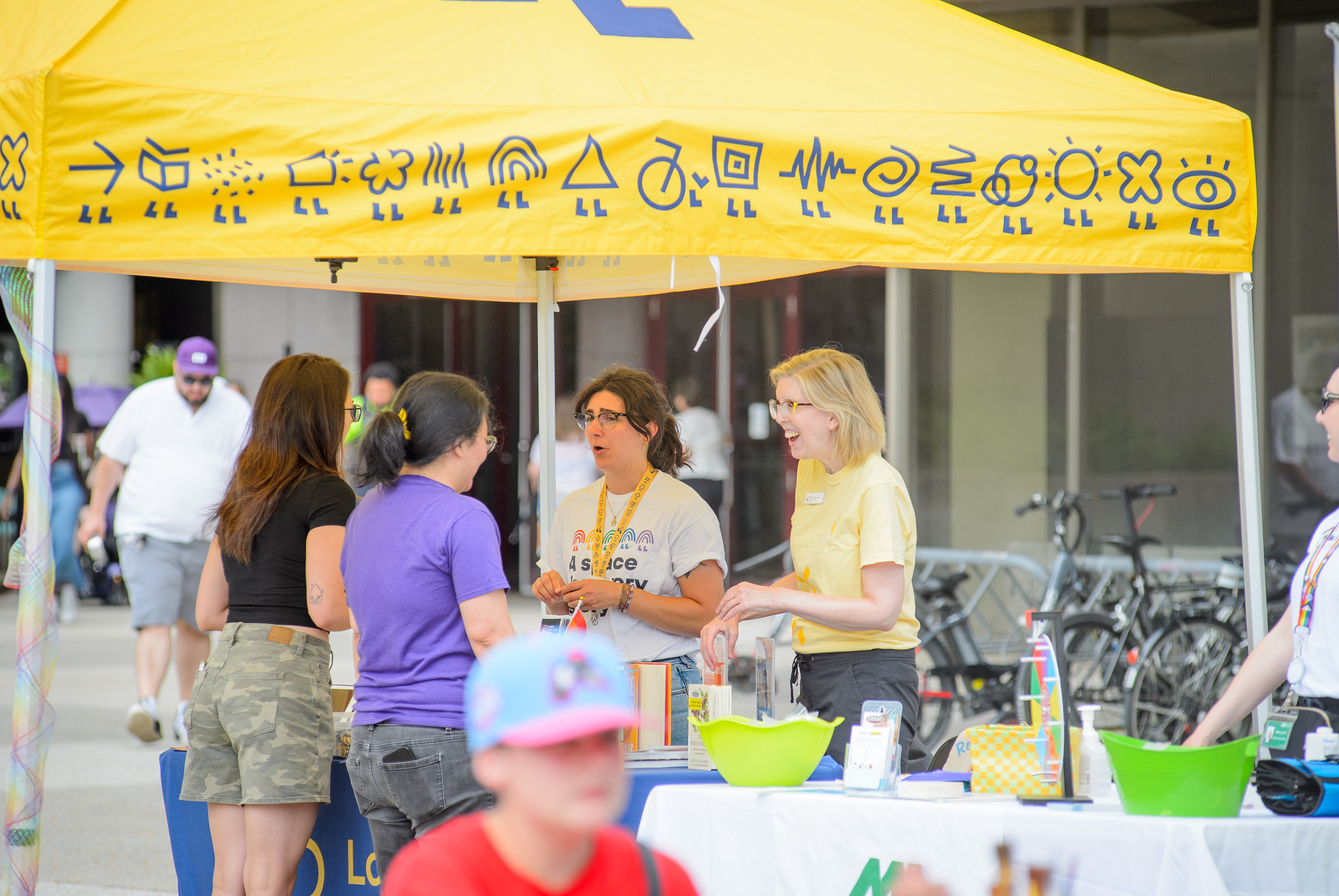 Two people at a yellow resources booth chat with people on the other side. 