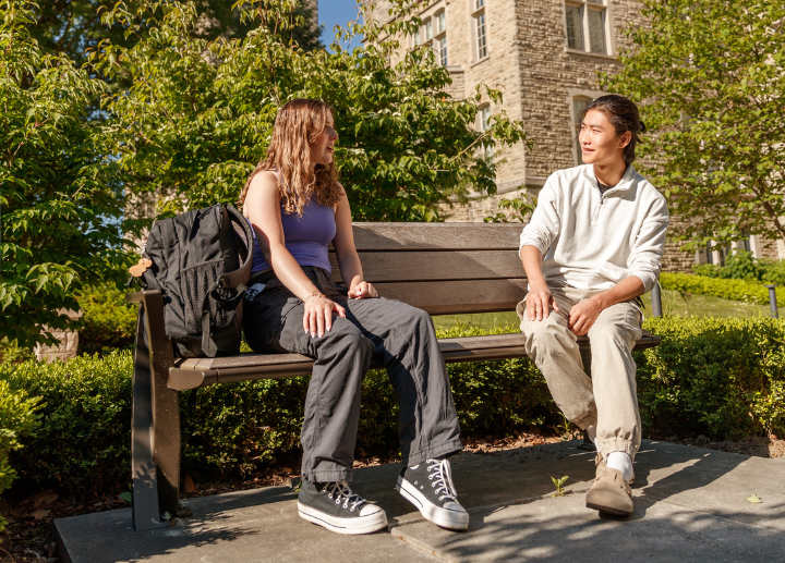 Two people sitting on a bench talking on campus