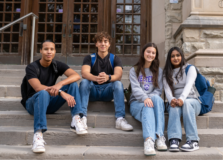 Four students sitting on the front entryway steps of a campus building