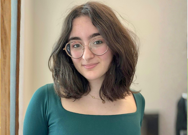 A photo of Emma Bullerwell with brown hair, wearing a teal shirt and glasses.