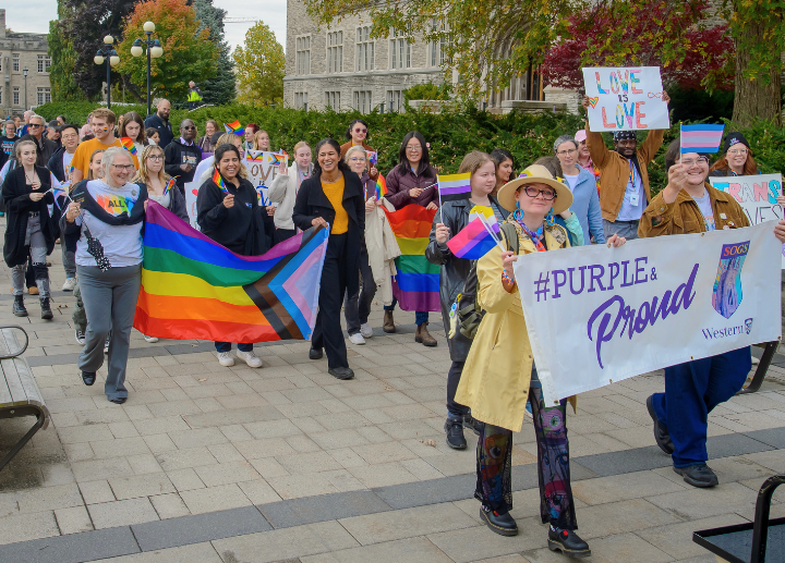 A photo of diverse people walking in last year's Fall Pride Parade, wearing colourful clothing and holding inclusive signs.