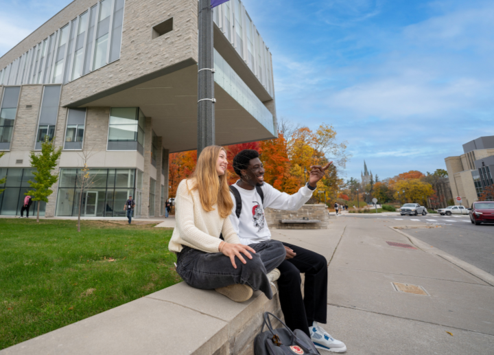 Two students pointing toward the air, sitting down.