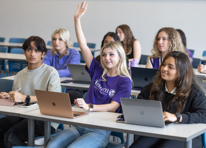 Students in a classroom wearing Western merchandise, with a young woman raising her hand in the front row ready to answer a question